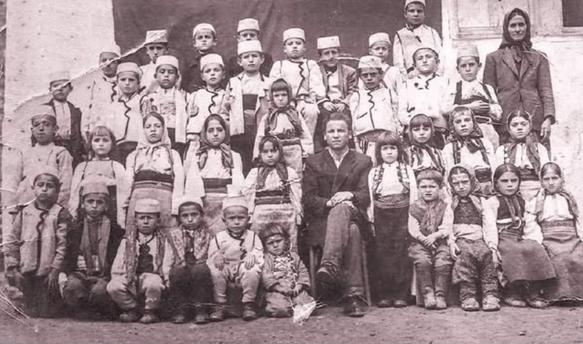Mësuesi Mahmut Dumani me nxënësit e tij, të veshur me kostume tradicionale dhe Plisin e bardhë, një fotografi që rrëfen sa shumë lidhet arsimi me trashëgiminë kulturore